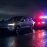 Modern electric SUV on a dark highway surrounded by flashing emergency lights.